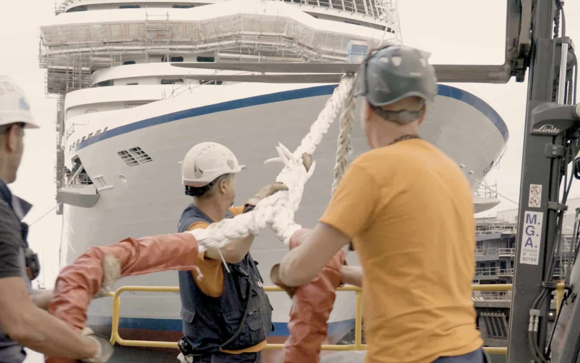 Ship yard workers hold ropes securing Oceania Cruises new Allura ship.