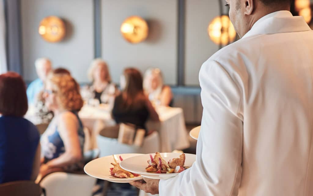 A waiter with a plate of food in Osteria d’Ovidio restaurant on a Crystal crusie ship.